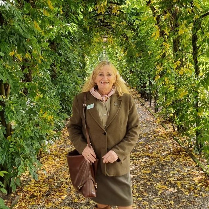 Irene Beaupain lachend in een bladerpergola met herfstbladeren op het pad